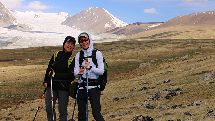 Hikers trekking in the Altai Mountains of western Mongolia with glacier views in the background, enjoying high-altitude adventure and stunning alpine scenery.